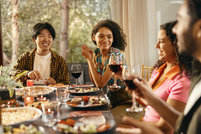 Happy friends enjoying in conversation and drinking wine during festive dinner at home party